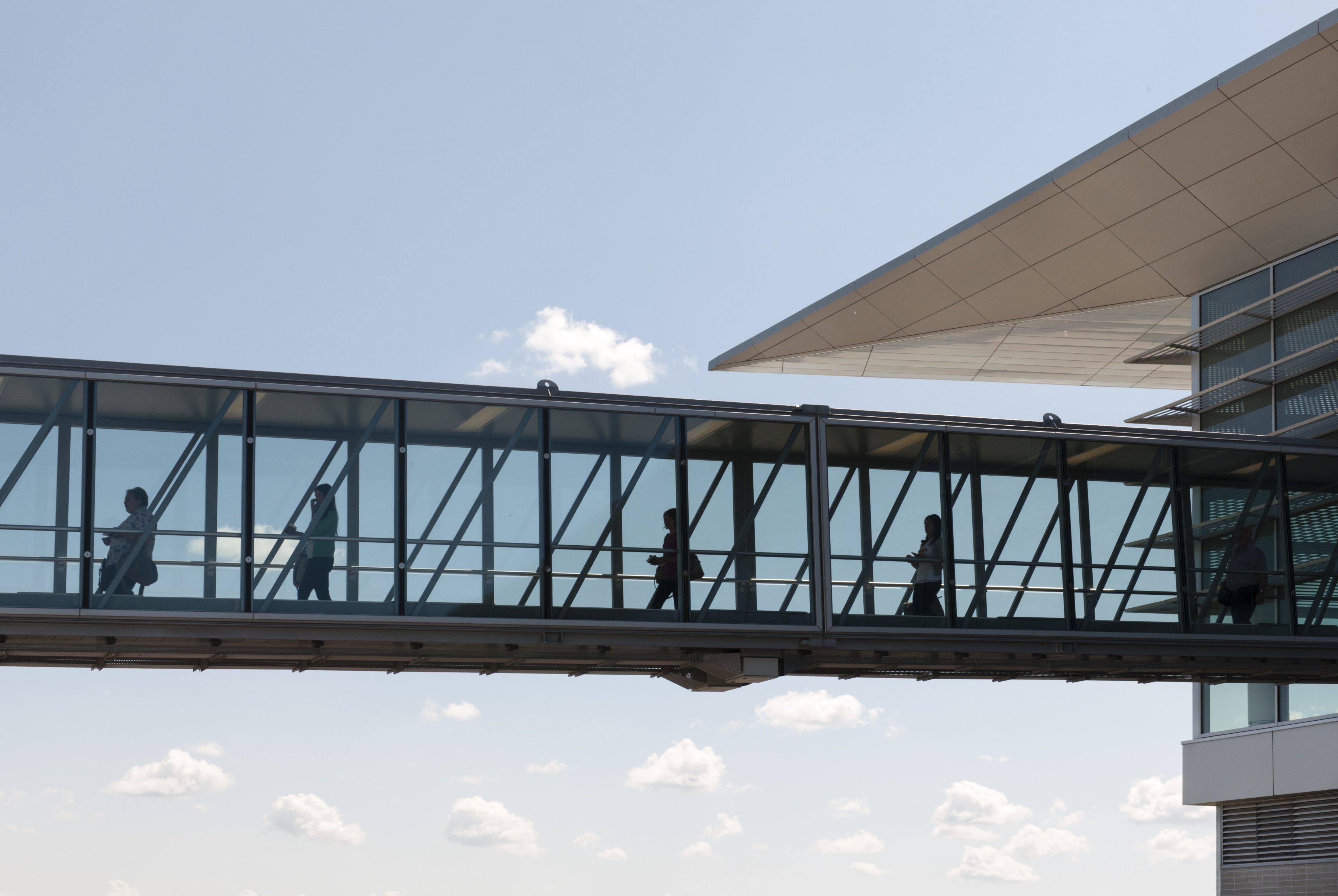 In a picture taken outside, travellers are shown walking away from the terminal and down one of the glass-walled boarding bridges at Winnipeg Richardson International Airport.