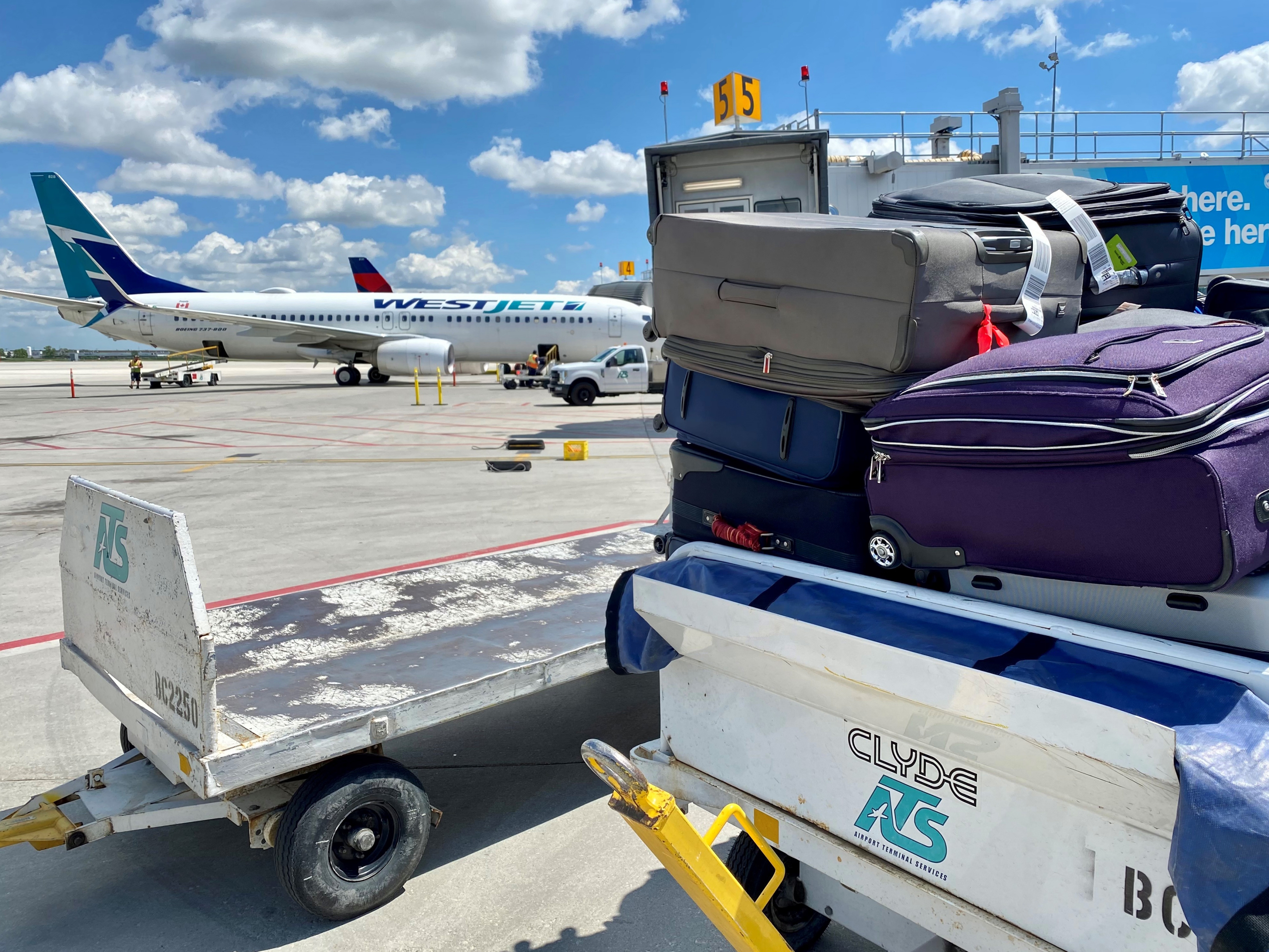 Bags are stacked on a luggage cart, waiting to be loaded on a plane with a WestJet aircraft in the background.