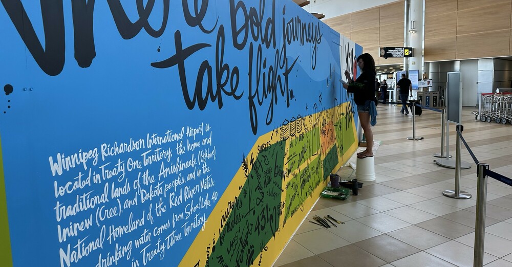 Famed Winnipeg artist Kal Barteski stands on an upside-down five-gallon pail as she paints a mural on the Departures Level of the Winnipeg Richardson International Airport terminal.
