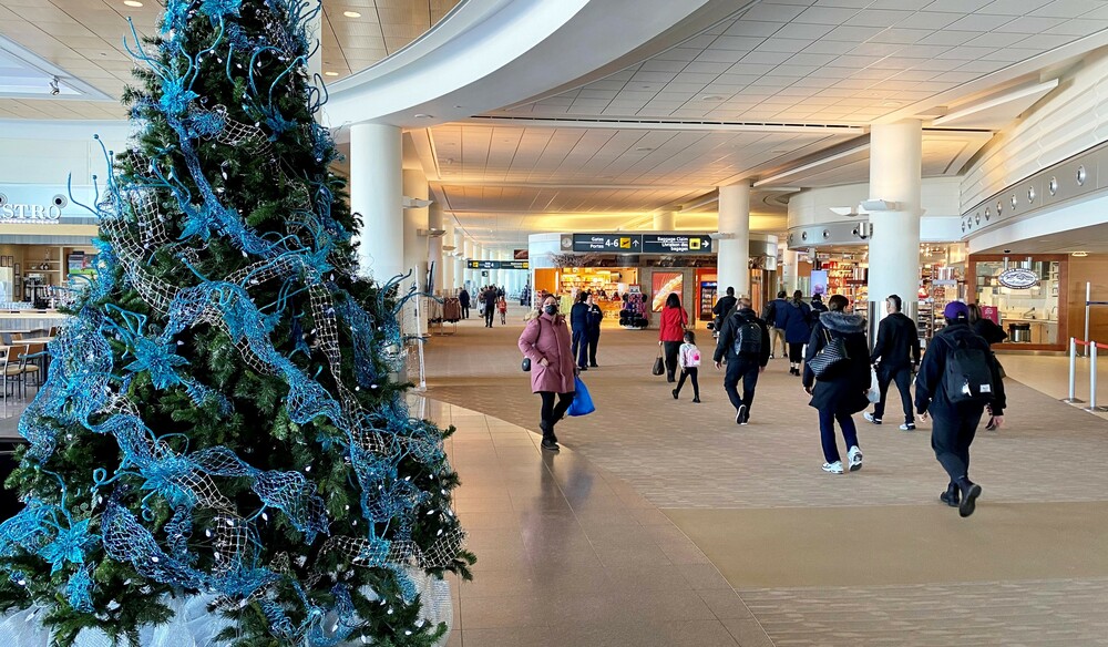 Des voyageurs passent devant un arbre décoré pour les Fêtes dans la zone des portes d'embarquement des vols intérieurs et internationaux de l'aéroport international Richardson de Winnipeg.